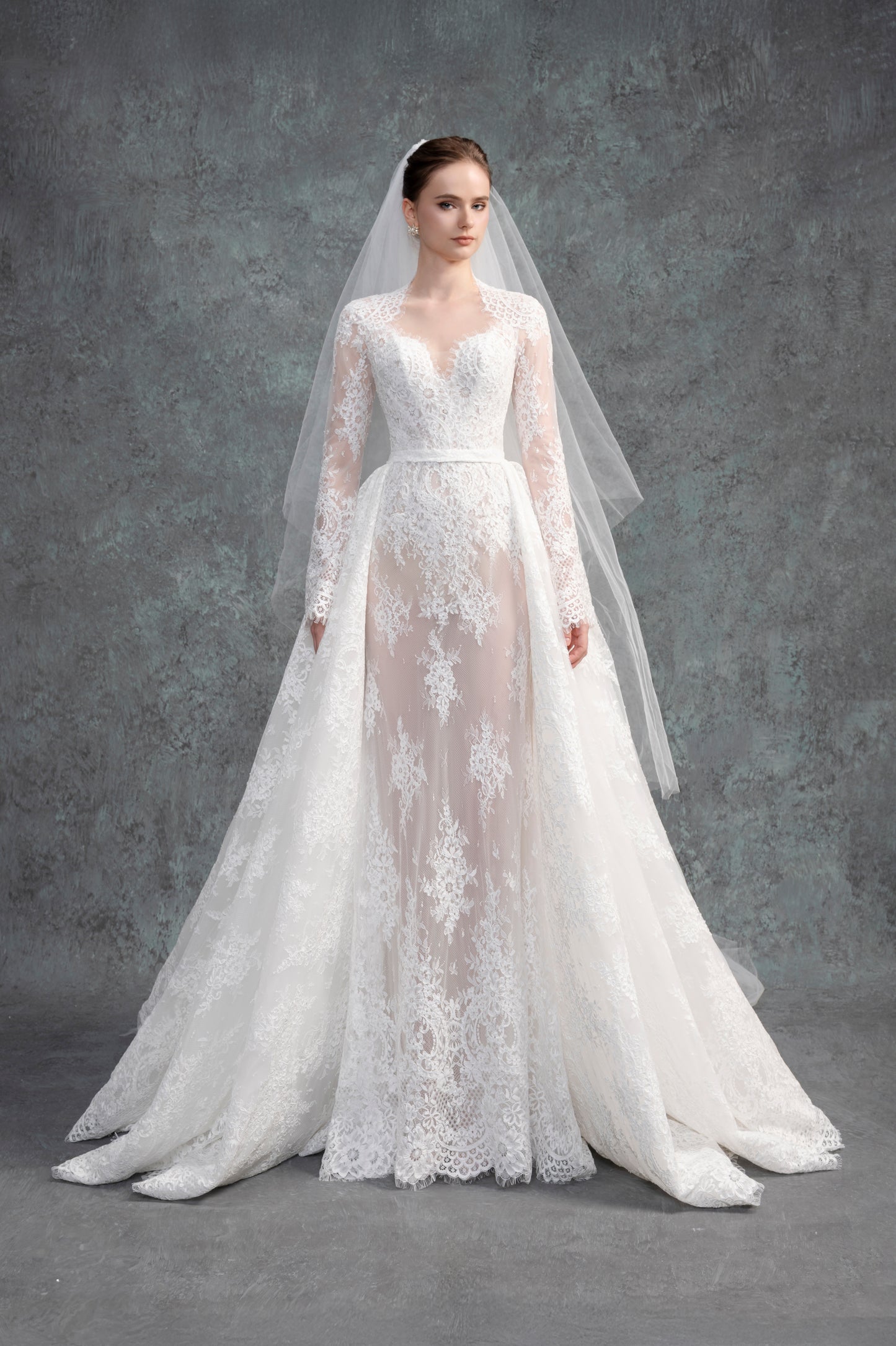 White lace wedding dress with long sleeves and a matching veil on a gray background