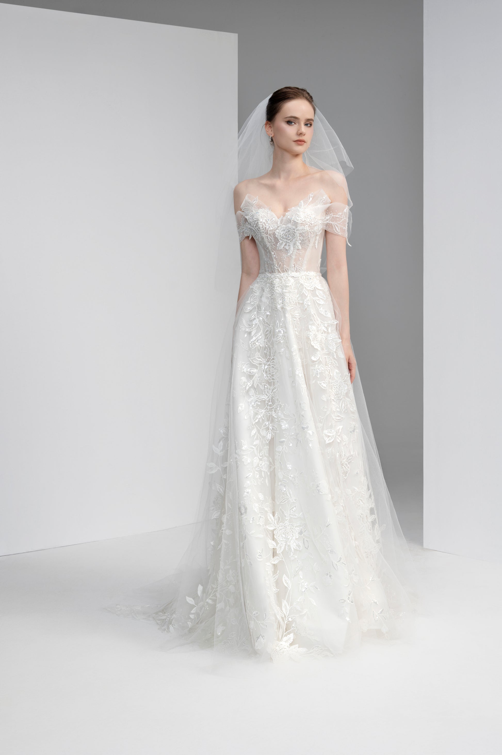 Model wearing a white lace wedding dress with a veil against a plain background