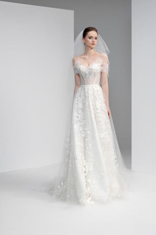 Model wearing a white lace wedding dress with a veil against a plain background