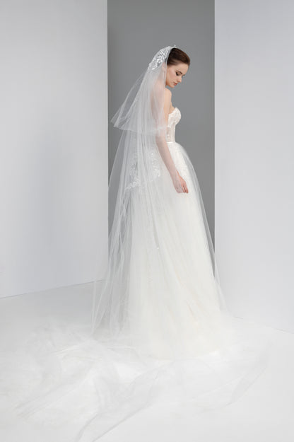 Woman wearing a white wedding dress with a long veil against a gray background