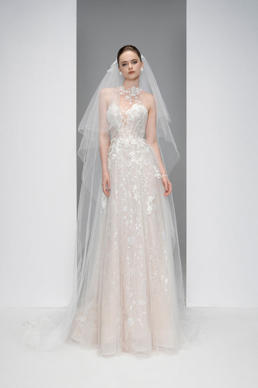 Model wearing a white wedding dress with floral details and a long veil on a plain background