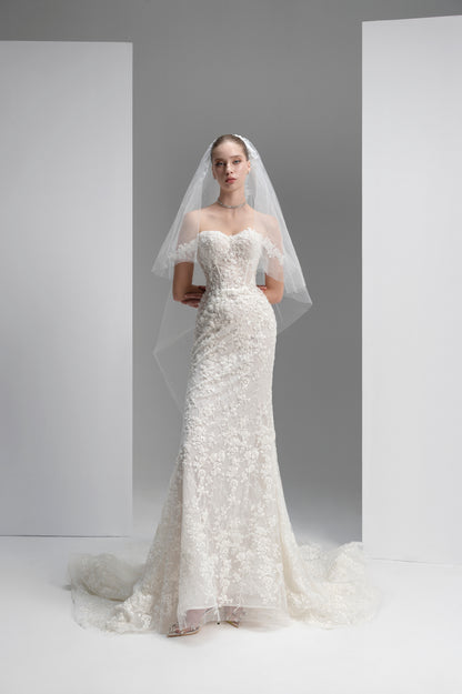 Model wearing a white lace wedding dress with a veil against a plain background