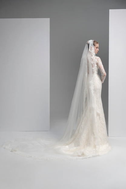 Bride in a white wedding dress with a long veil standing against a plain background