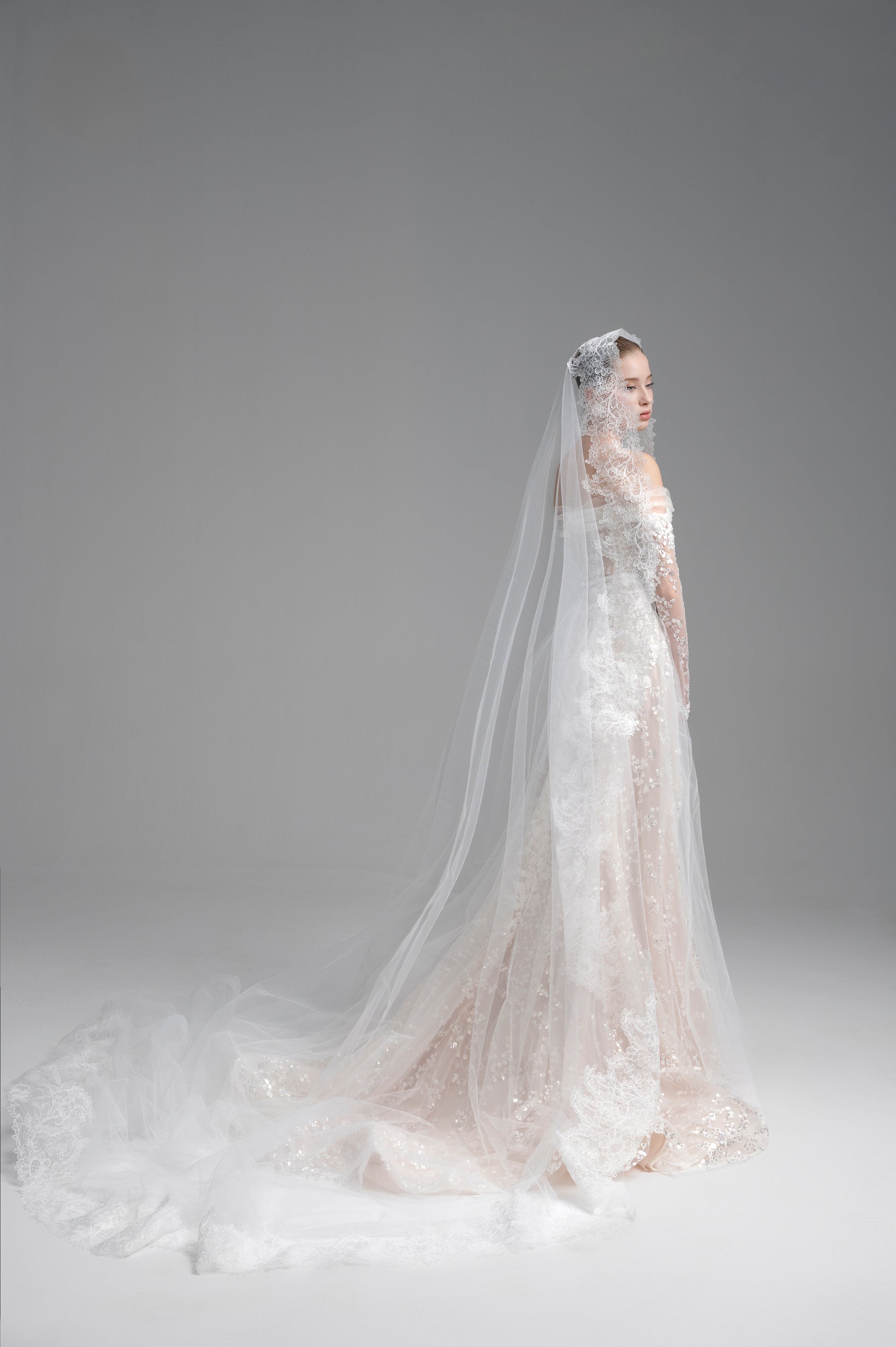 Bride in a white wedding dress with a long veil against a gray background