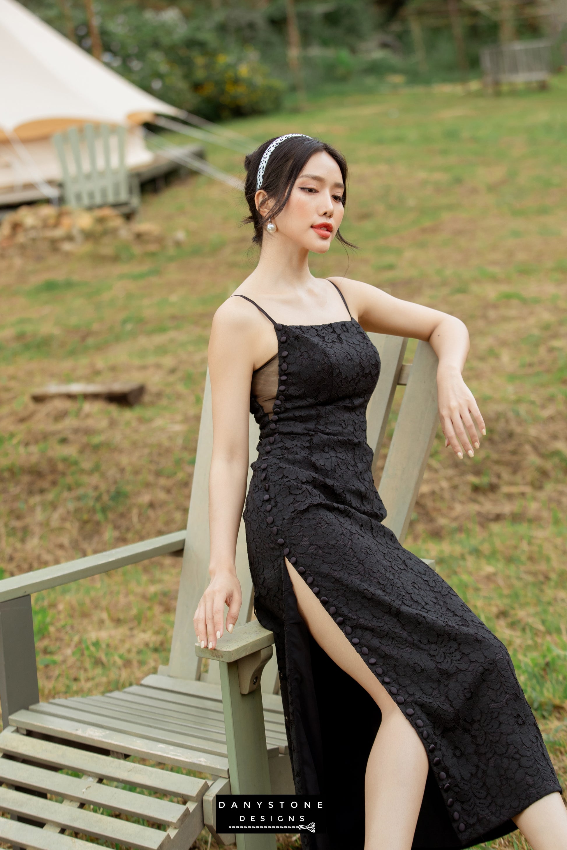 Model showcasing a black lace dress with slit and wrapped buttons in a natural setting