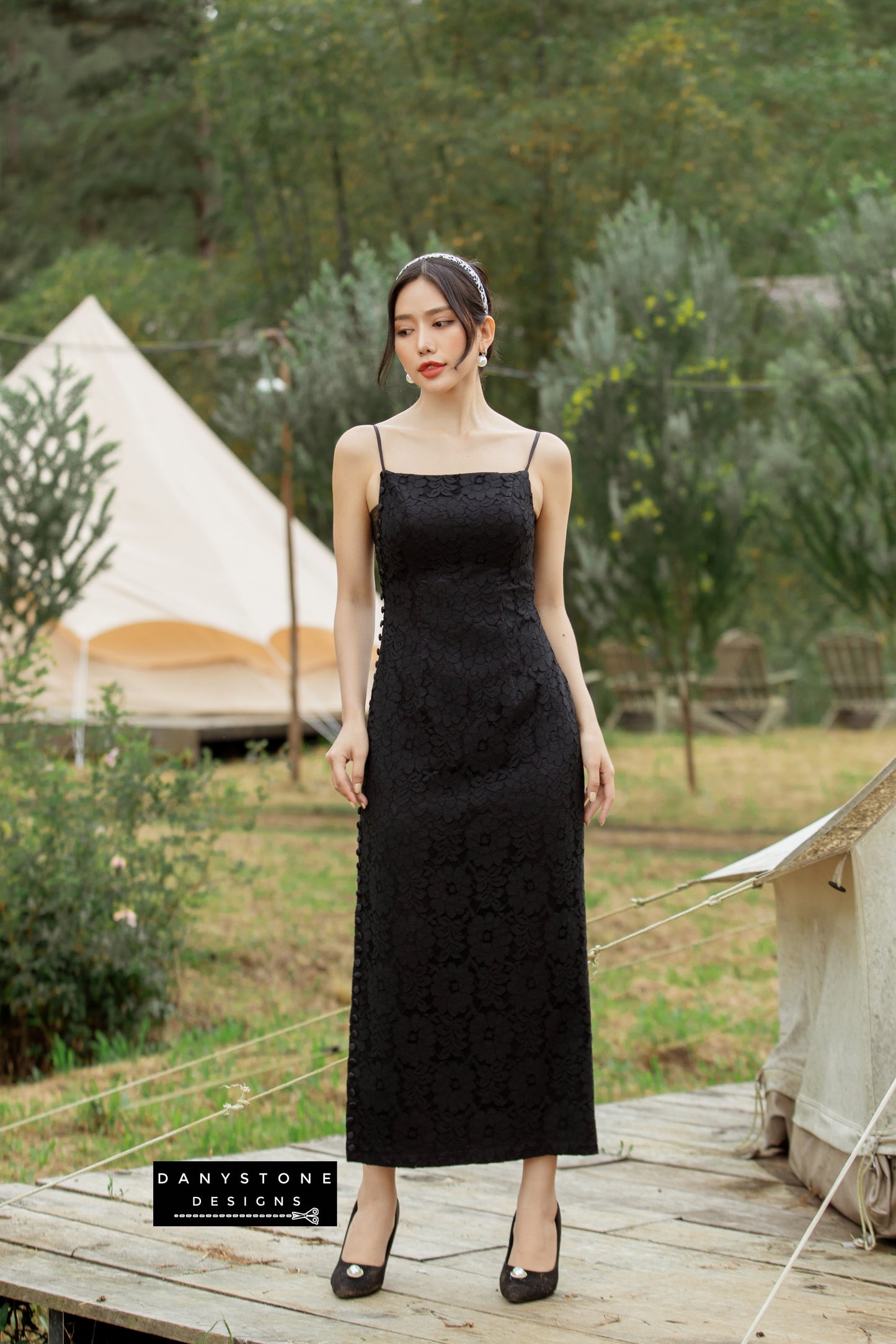 Black lace dress with satin accents and wrapped buttons worn by a model in a natural setting