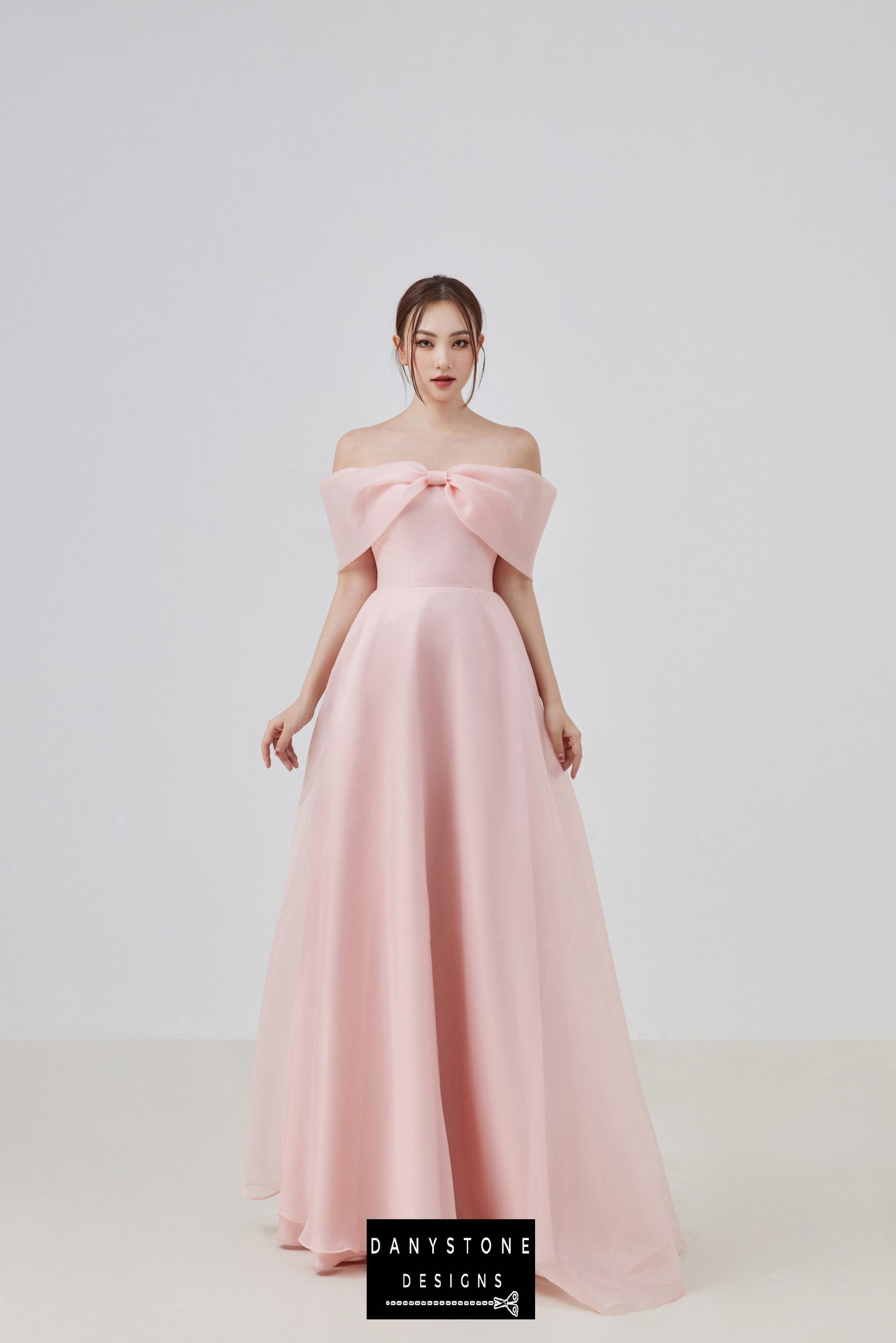 Model wearing an elegant pink off-shoulder silk chiffon dress with a bow