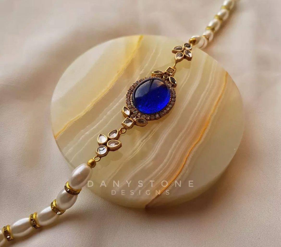 Indo-Western fusion necklace with a blue sapphire-like stone surrounded by small rhinestones, displayed on a round, striped stone background.