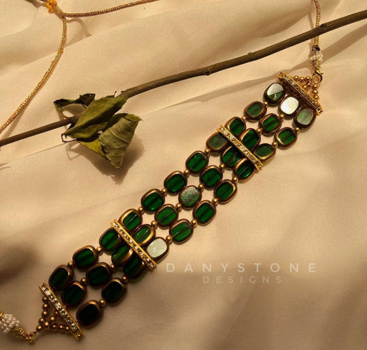 Bottle green statement choker with gold-toned framework and intricate design, displayed on a soft beige fabric background with a twig.