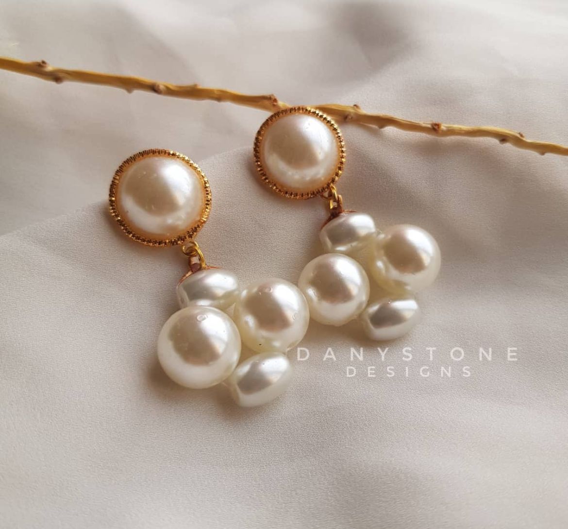 Handcrafted vintage pearl drop earrings with a cluster of pearls hanging from a gold-toned base, displayed on a soft beige fabric background.