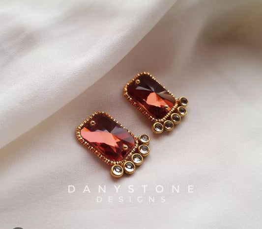 Handcrafted coral pink crystal stud earrings with polki-like stones, displayed on a soft beige fabric background.