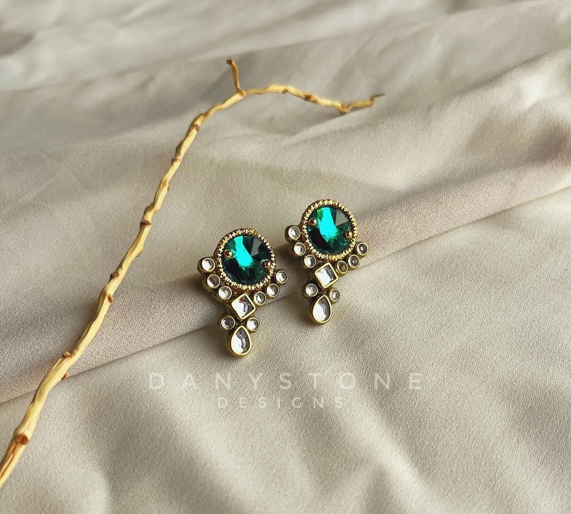 Handcrafted bottle green Swarovski crystal earrings with polki-like stones, displayed on a soft beige fabric background.