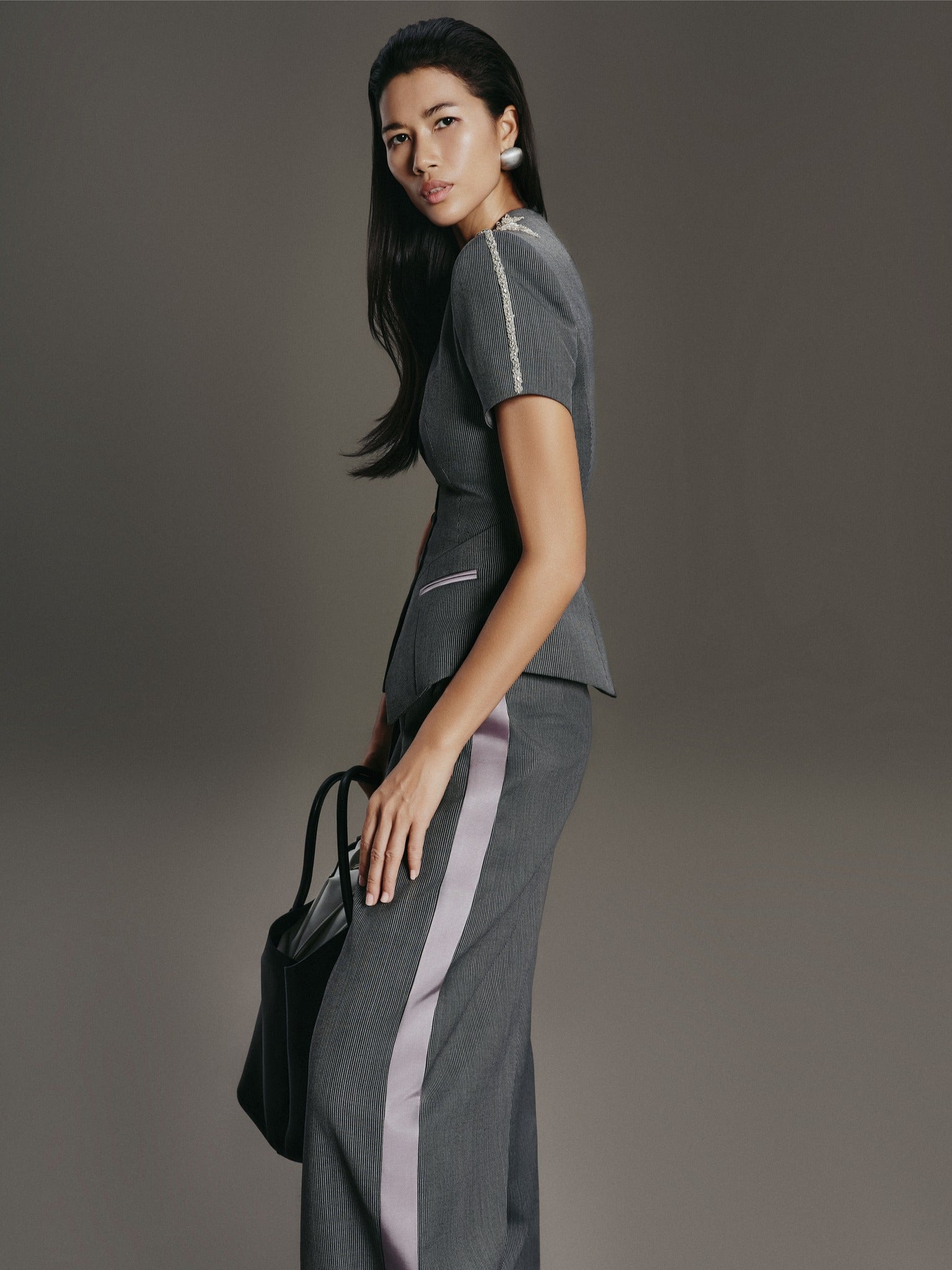 Woman in a gray outfit with a black handbag against a gray background