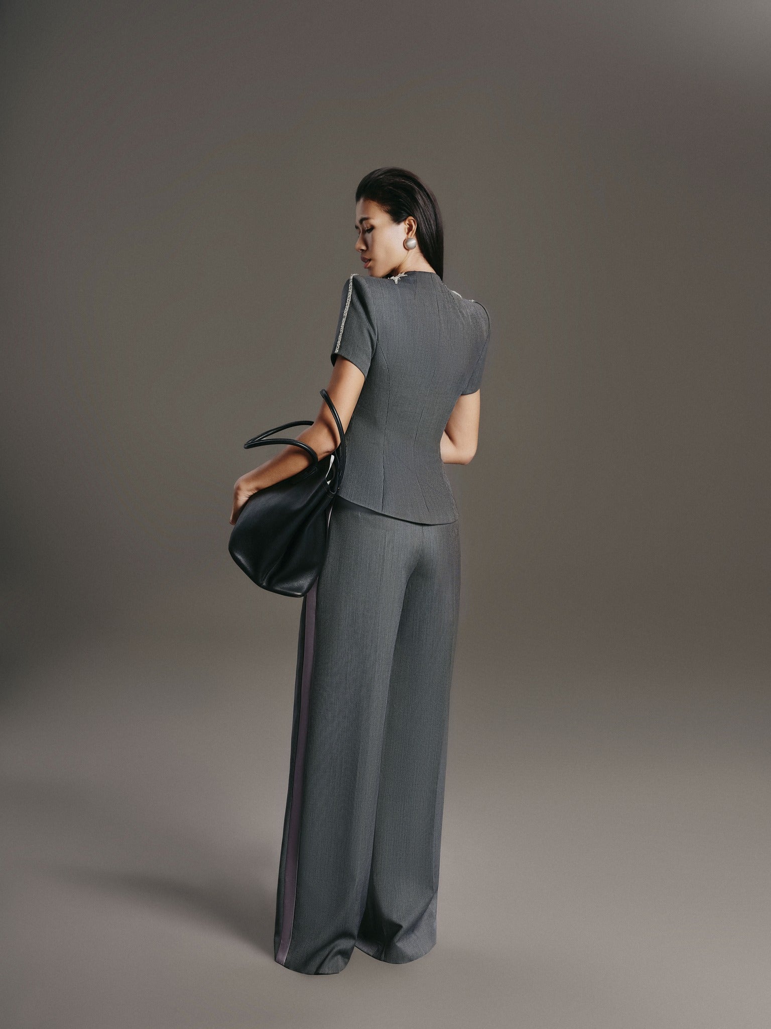 Woman in a gray outfit holding a black handbag against a gray background