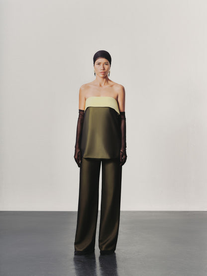 Woman wearing a two-tone outfit with a green top and wide-leg pants on a plain background