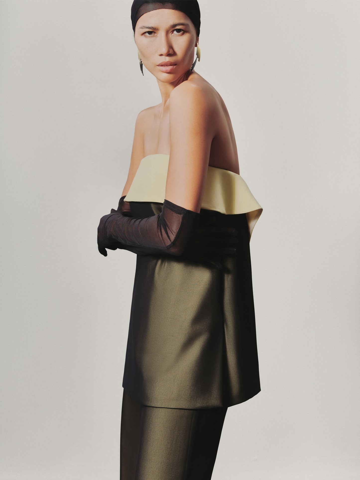 Woman wearing a gold and black off-shoulder top with a plain background