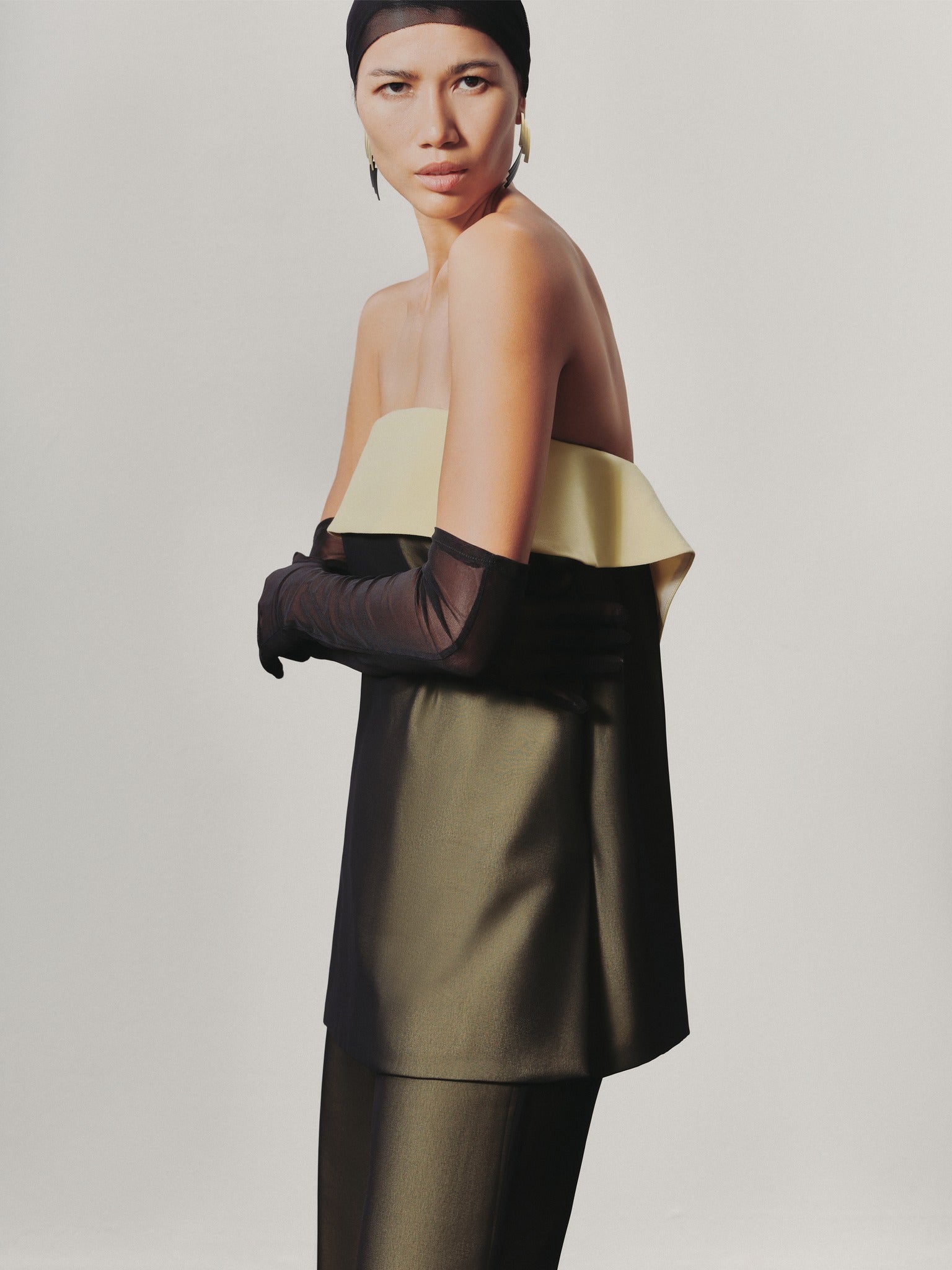 Woman wearing a gold and black off-shoulder top with a plain background