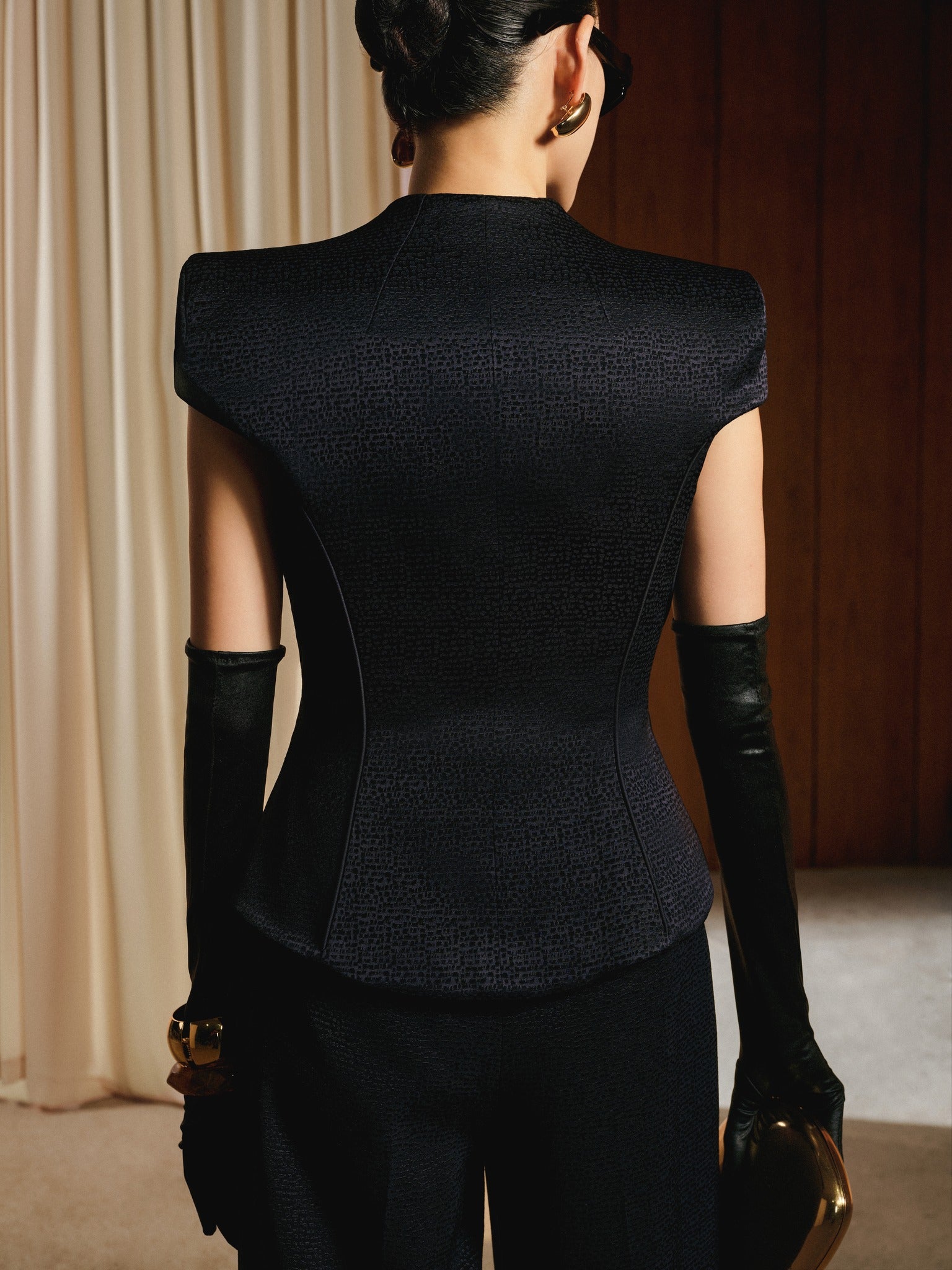 Person wearing a black outfit with long gloves in a room with beige curtains.