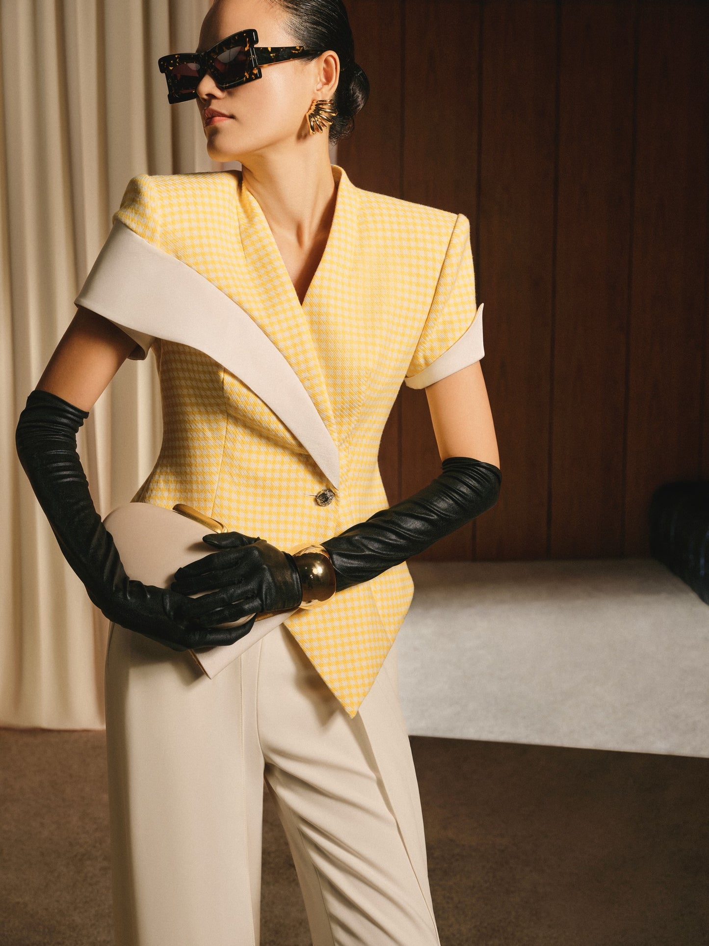 Person wearing a yellow checkered outfit with black gloves and sunglasses indoors.