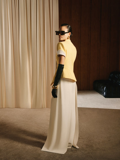 Person wearing a yellow top and white pants standing in a room with beige curtains and a wooden wall.