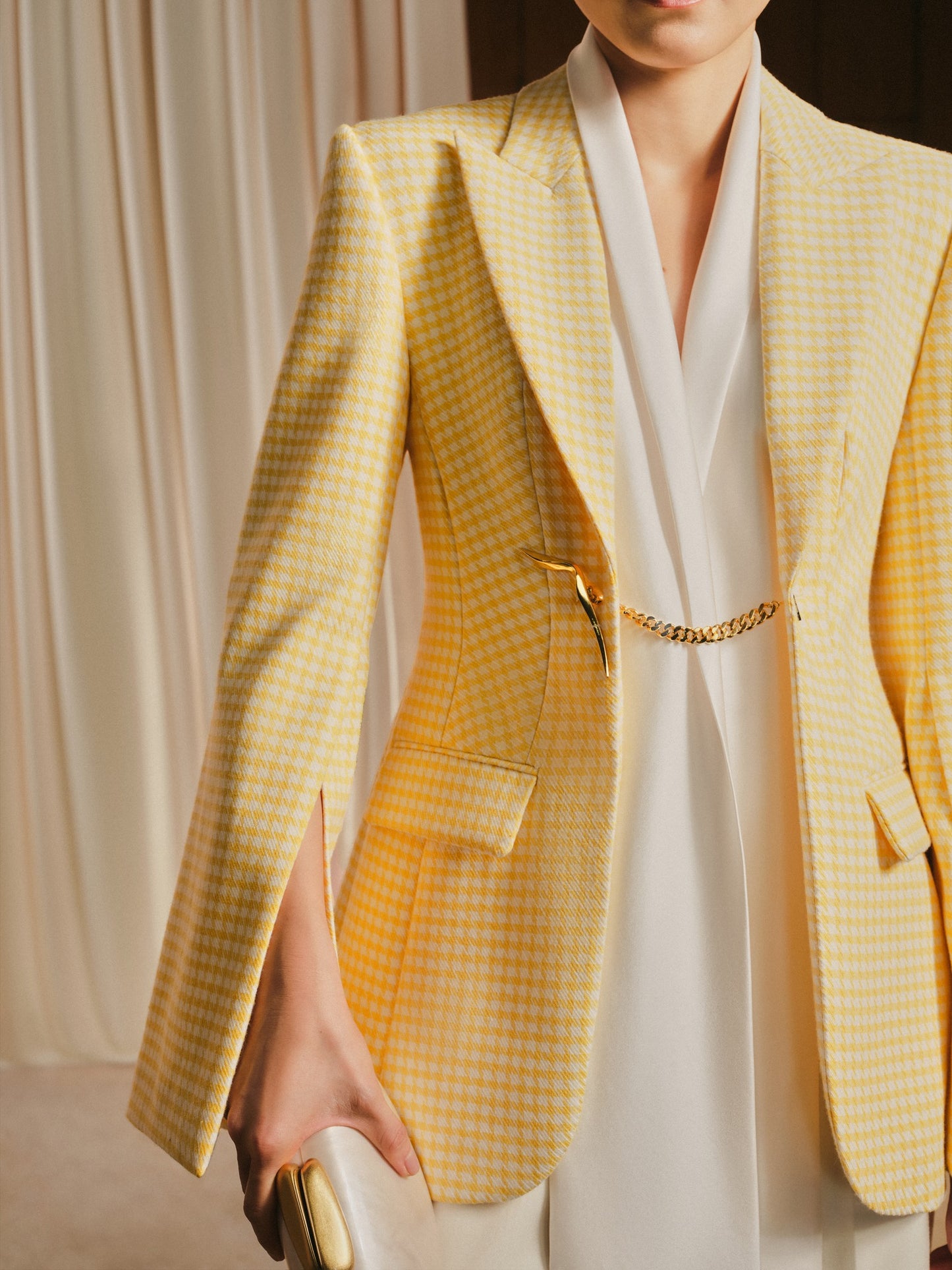 Person wearing a yellow checkered blazer over a white outfit with a gold belt.