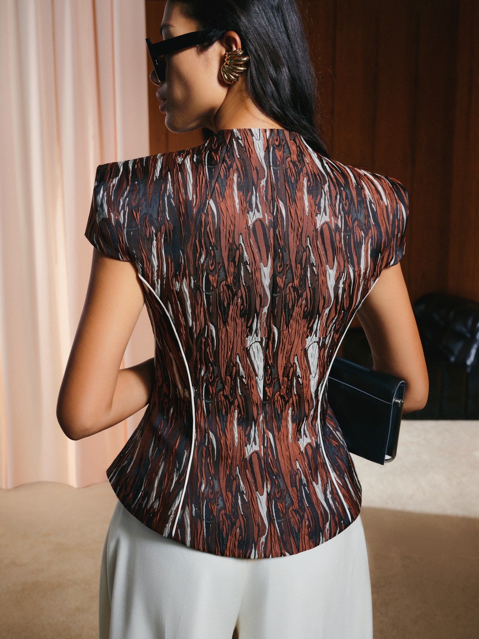 Woman wearing a patterned top and sunglasses, holding a clutch.