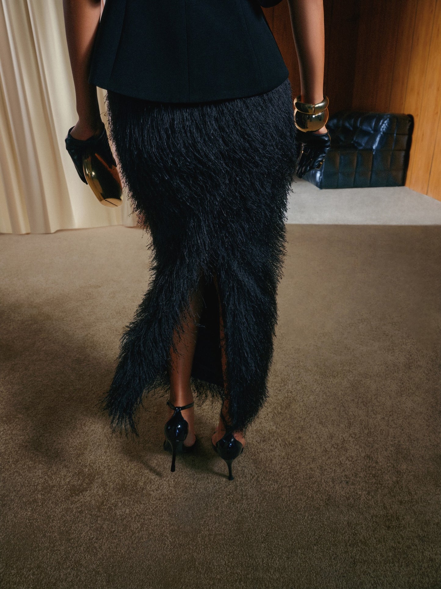 Person wearing a black feathered skirt and high heels in an indoor setting.