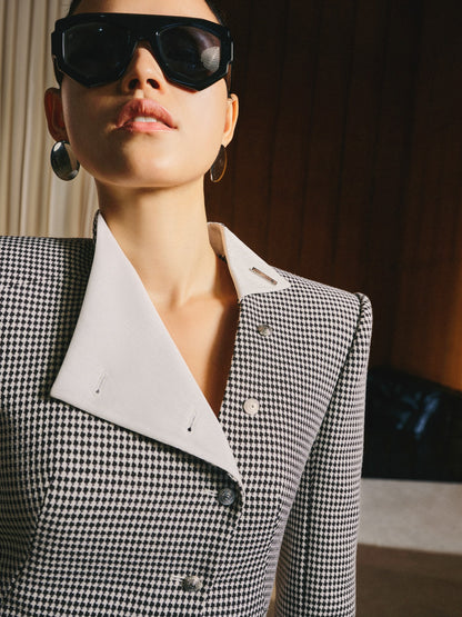 Person wearing a black and white checkered blazer with sunglasses indoors.