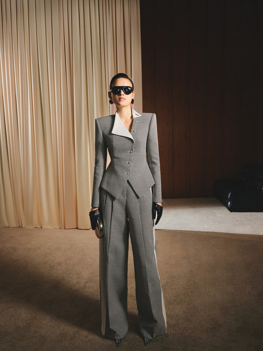 Woman in a gray suit standing in a room with beige curtains and a dark floor.