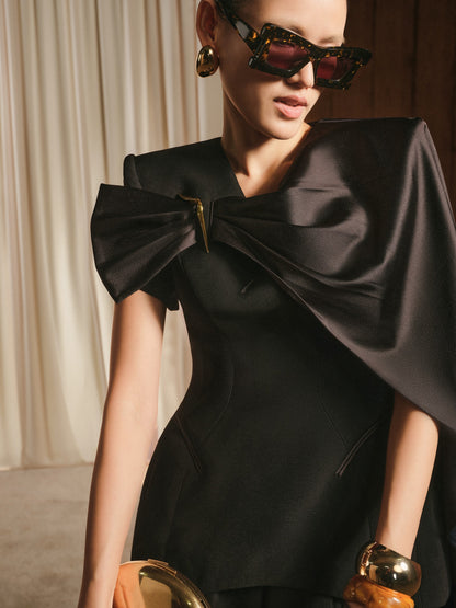 Woman wearing a black dress with a large bow and sunglasses indoors.