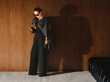 Person in a black outfit standing against a wooden wall with a leather chair.