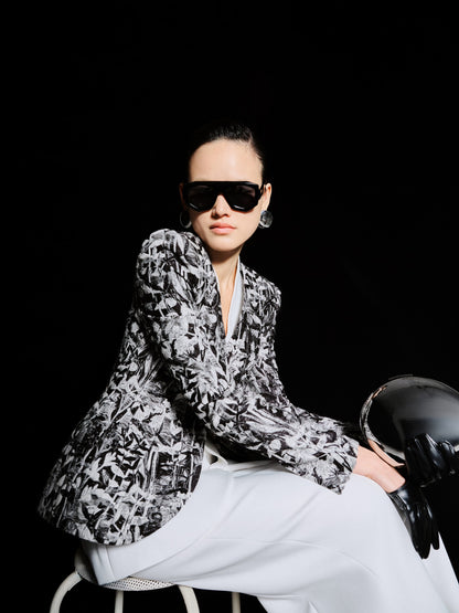 Person wearing a patterned blazer and sunglasses against a black background