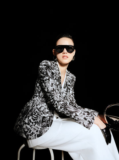 Person wearing a patterned blazer and sunglasses against a black background