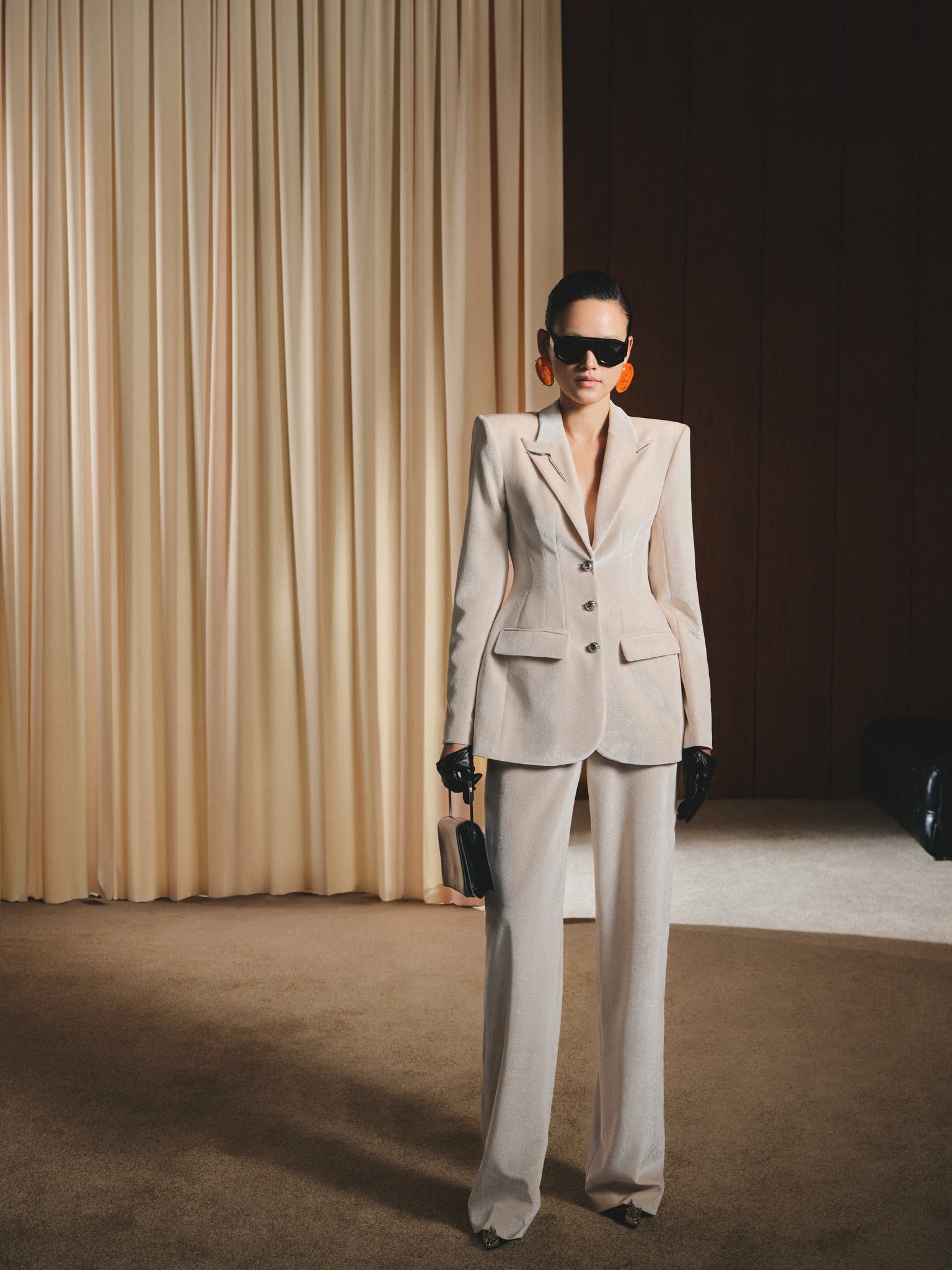 Woman in a beige suit standing in front of a curtain