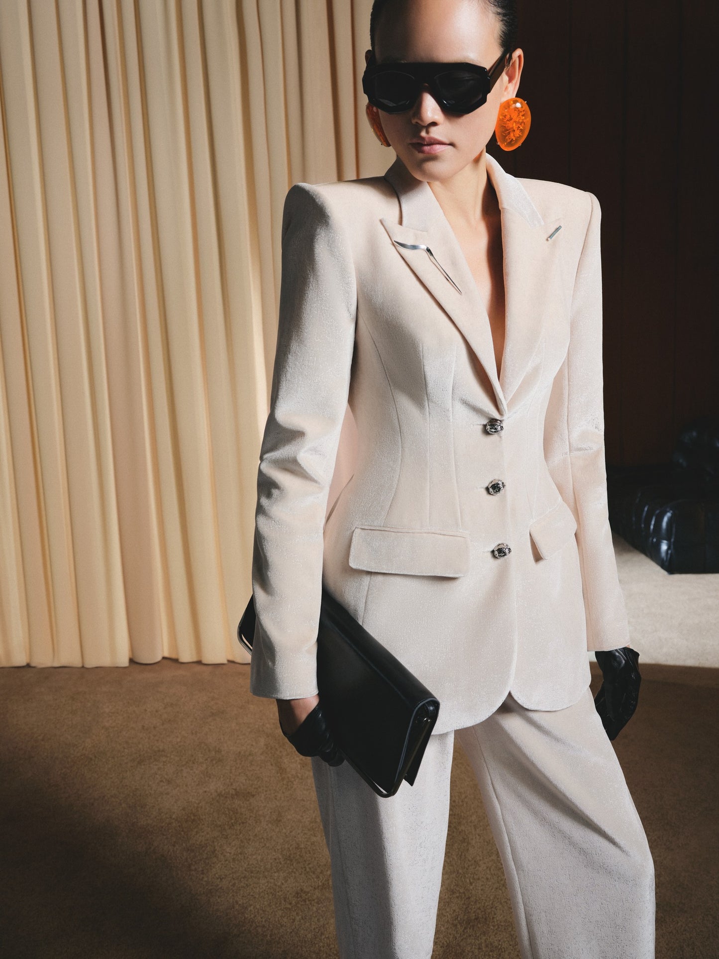 Person wearing a beige suit with sunglasses and gloves against a neutral background