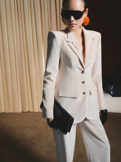 Person wearing a beige suit with sunglasses and gloves against a neutral background