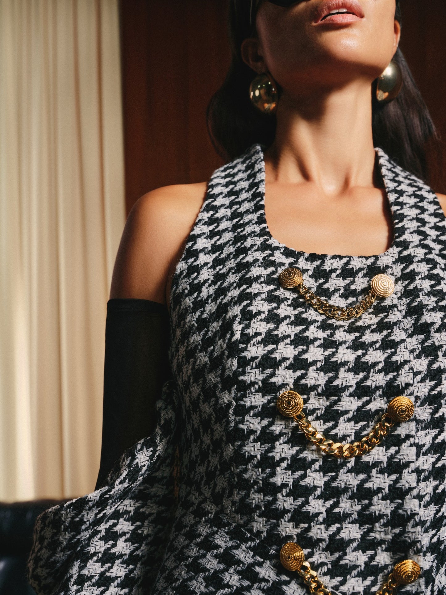 Woman wearing a black and white houndstooth patterned dress with gold buttons and a necklace.