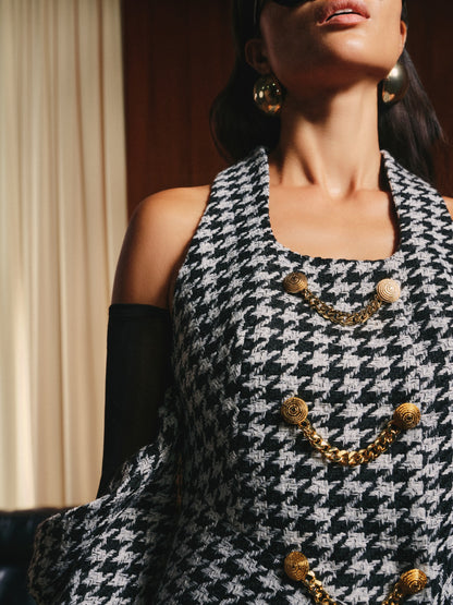 Woman wearing a black and white houndstooth patterned dress with gold buttons and a necklace.