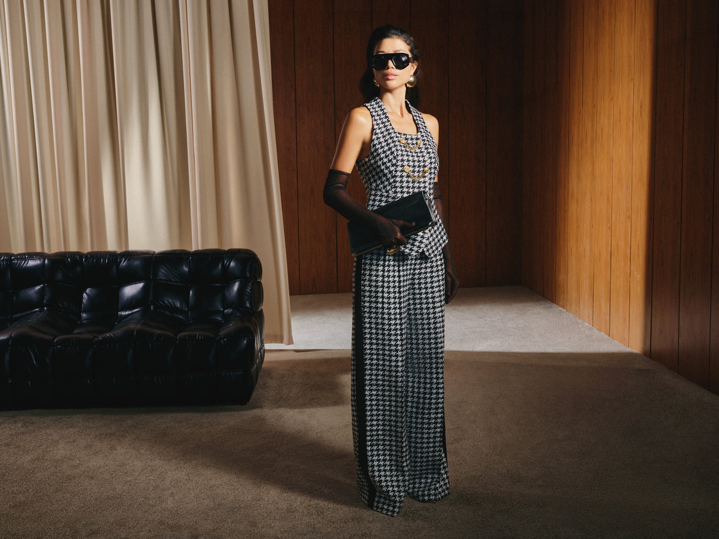 Woman in a checkered dress standing in a room with a black leather couch and wooden walls.