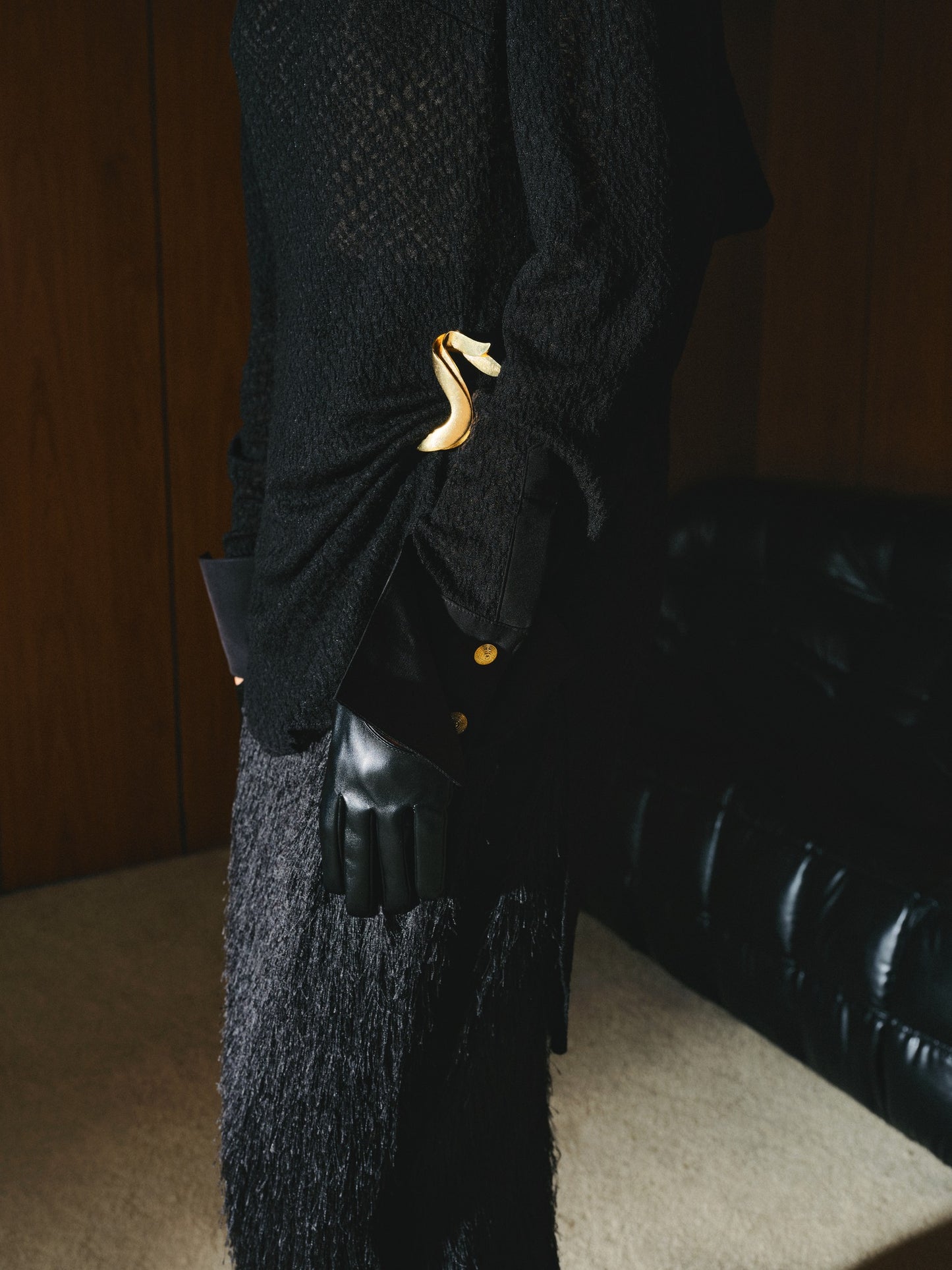 Black textured coat with gold buttons on a mannequin against a dark background