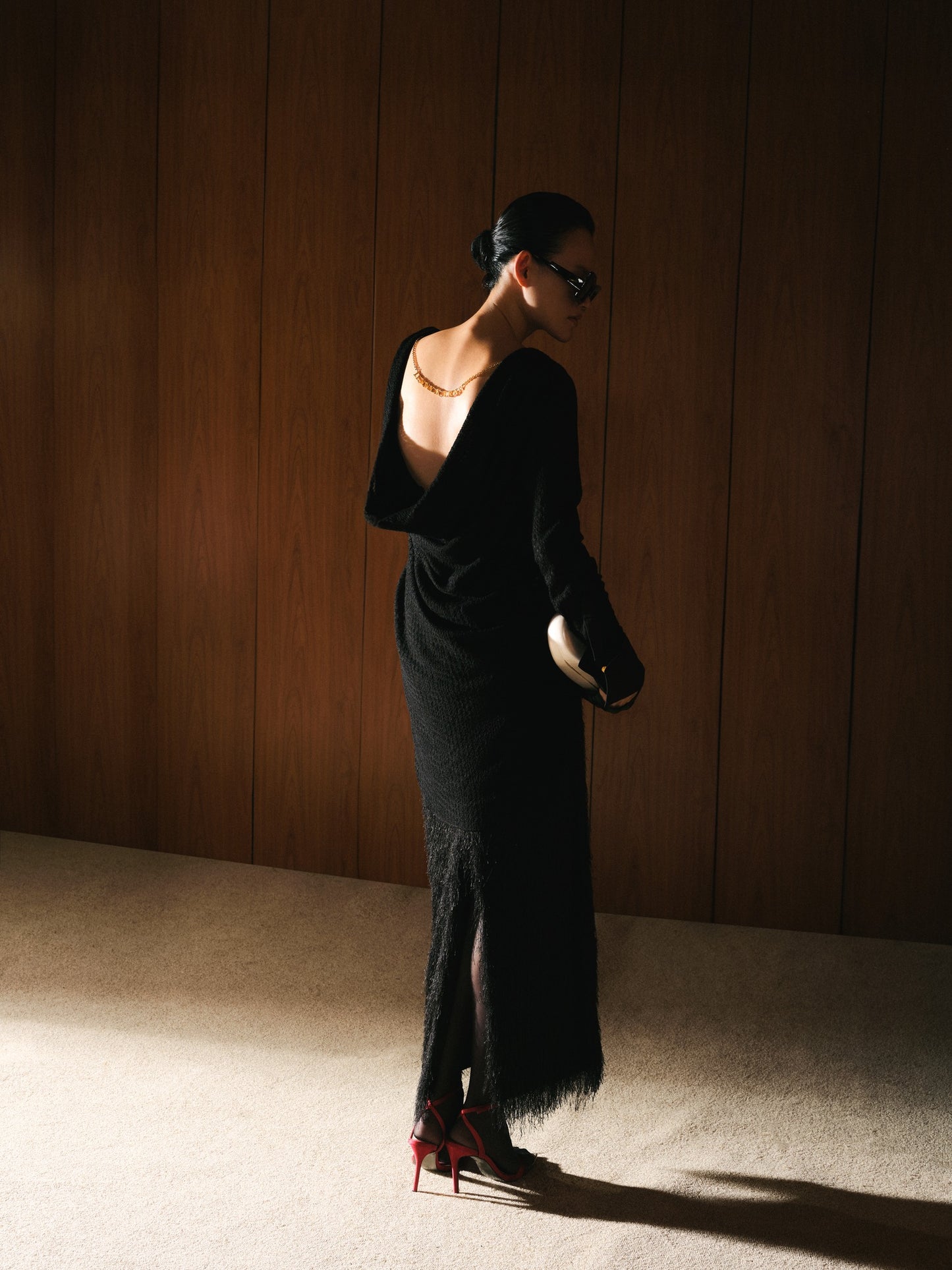 Woman in a black dress standing against a wooden paneled wall.