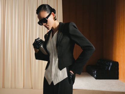 Woman in a stylish outfit with a black jacket and sunglasses in an indoor setting.