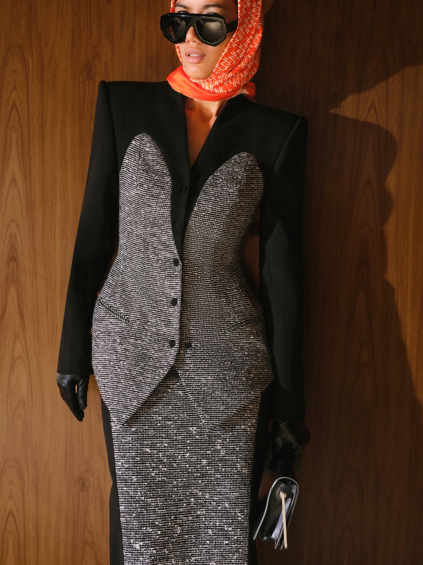 Person wearing a black blazer over a silver dress with a red headscarf against a wooden background