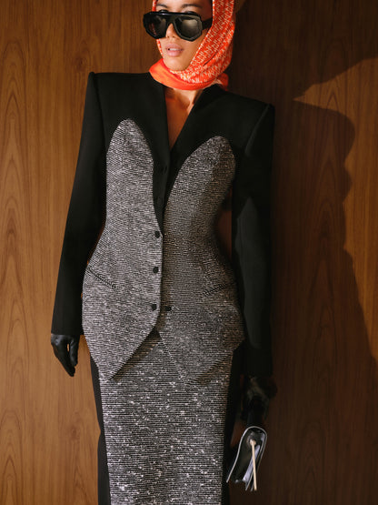 Person wearing a black blazer over a silver dress with a red headscarf against a wooden background