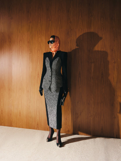 Person wearing a black and gray outfit with a scarf, standing against a wooden wall.