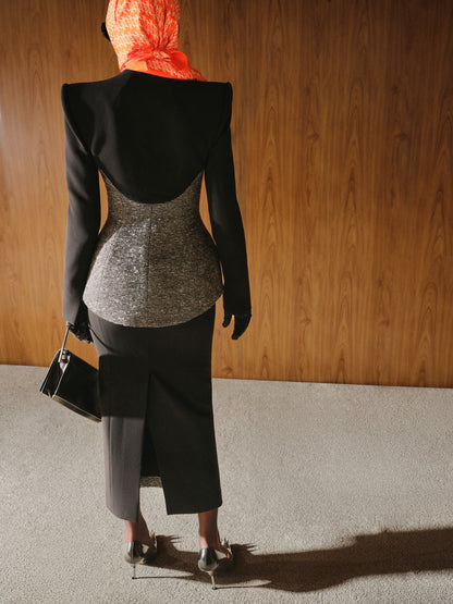 Person wearing a black outfit with a gray top and red headscarf, standing against a wooden wall.