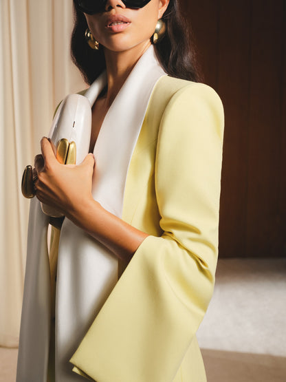 Woman in a yellow blazer and white top holding a gold object.