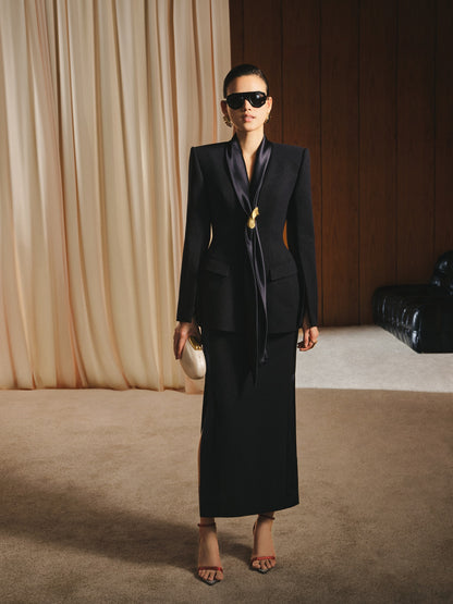 Woman in a black suit with a long train standing in front of a curtain.