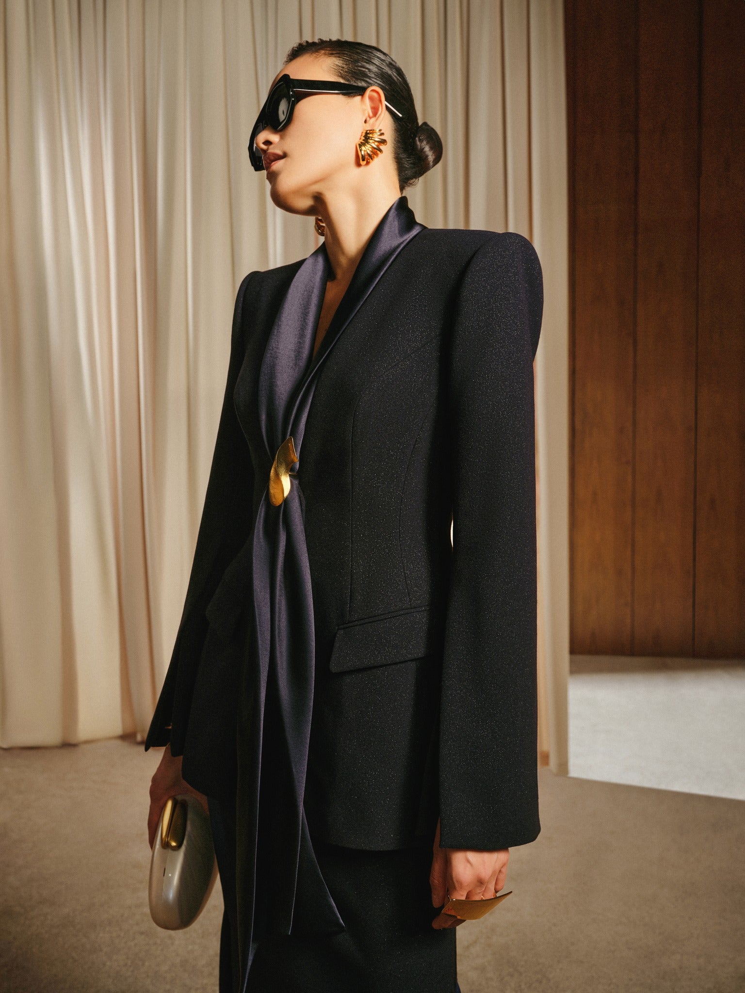 Person wearing a black suit with a long dark scarf, standing against a neutral background.