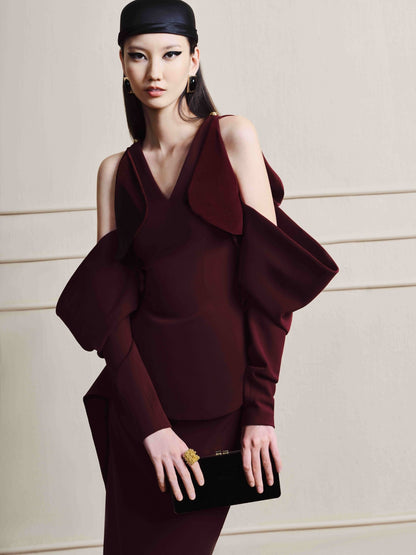 Woman wearing a burgundy dress with a black clutch against a neutral background